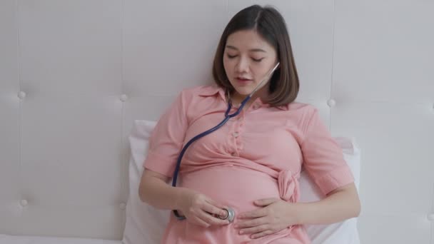 Молодая Беременная Азиатка Используя Стетоскоп Слушает Свое Нерожденное Детское Движение — стоковое видео