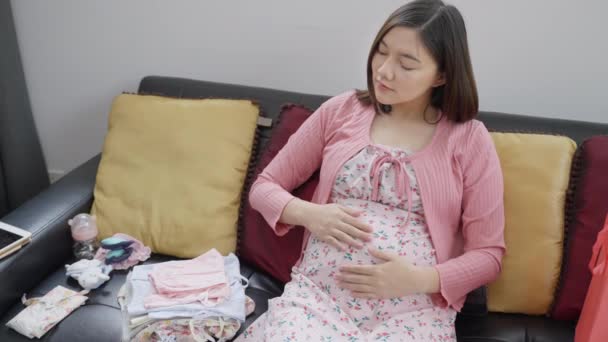 Счастливая Молодая Беременная Азиатка Сидит Дома Диване Смотрит Недавно Приобретенную — стоковое видео