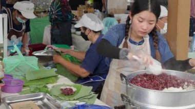 Chiang Mai, Tayland - 28 Mayıs 2023 - Genç kadın yiyecek satıcısı buharlı pirinci konteynırdan çıkarıp Greenheart sabah pazarındaki müşterisi için muz yaprağına sarar.