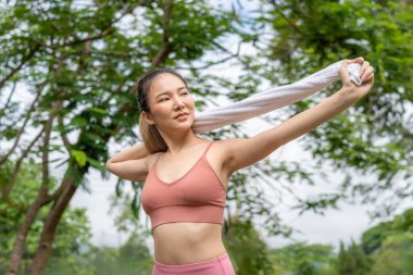 Genç ve çekici Asyalı kadın sabah egzersizinden önce kollarını ve bacaklarını uzatarak yerel bir parkın koşu pistinde koşuyor.