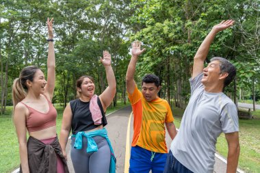 2 erkek ve 2 kadın koşucudan oluşan bir grup, yerel bir parkın koşu pistindeki başarılarını kutlamak için ellerini havaya kaldırdı.