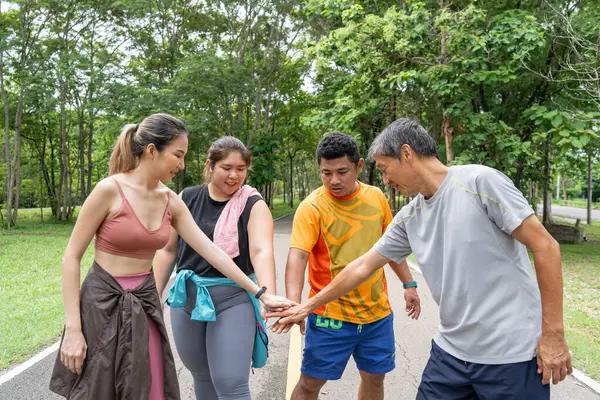 2 erkek ve 2 kadın koşucudan oluşan bir grup, yerel bir parkın koşu pistinde koşma başarılarını kutlamak için ellerini birleştiriyor.