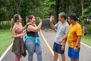 İki erkek ve iki kadın koşucudan oluşan bir grup, yerel bir parkın koşu pistindeki başarılarını kutlamak için birbirlerine beşlik çakıyor.