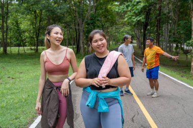 Sıska ve kilolu iki genç kadın, yerel bir parkın koşu pistinde sabah yürüyüşü yaparken birbirlerine eşlik etmekten zevk alırlar.