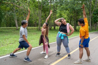 2 erkek ve 2 kadın koşucudan oluşan bir grup, yerel bir parkın koşu parkında koşmaya başlamadan önce vücut esneme hareketleri yapıyorlar.