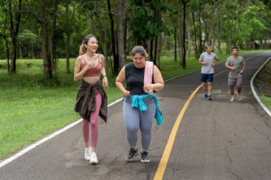 Sıska ve kilolu iki genç kadın, yerel bir parkın koşu pistinde sabah koşularında birbirlerine eşlik etmekten zevk alıyorlar.