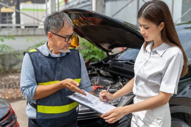 Bir araba sigortacısı, kadın müşteriye arka plandaki arabanın motorunun bulanık olduğu sigorta talep formunu nerede imzalayacağını gösteriyor.