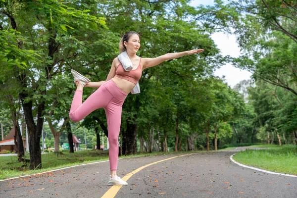 年轻迷人的亚洲女人在晨练前伸着胳膊和腿跑到当地一个公园的跑道上 免版税图库照片