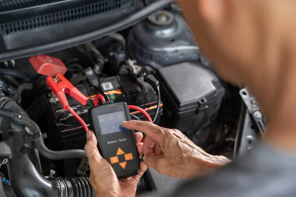 用电池测试仪紧紧抓住一名男性汽车修理工的手 检查汽车电池的状况 免版税图库照片