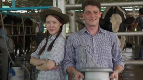 快乐的男女奶农在奶牛产奶场的奶牛产奶区前快乐地站着 — 图库视频影像