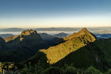 Gün doğarken Doi Luang Chiang Dao 'nun tepesinden ön planda ağaçlar ve çalılar ve arka planda güzel sıradağlar görünüyor.