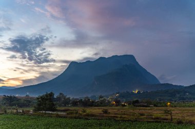 Akşam günbatımında Doi Luang Chiang Dao 'nun manzarası. Önde yeşil alan ve arkada dramatik bulutlar oluşmuş.