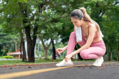 Genç ve çekici bir Asyalı kadın sabah egzersizinden önce ayakkabı bağcıklarını yerel bir parkta koşuyor.