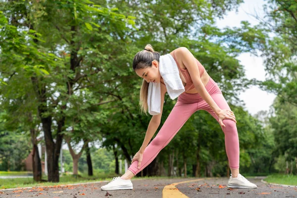 Genç ve çekici Asyalı kadın sabah egzersizinden önce kollarını ve bacaklarını uzatarak yerel bir parkın koşu pistinde koşuyor.