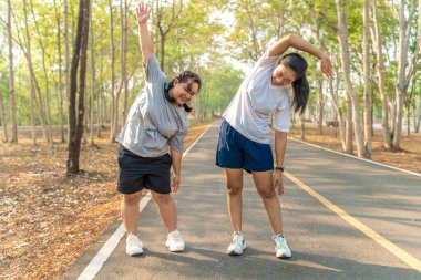 İki genç bayan arkadaş sabah koşularına başlamadan önce kollarını ve bacaklarını esnetiyorlar.
