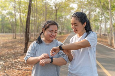 İki genç bayan arkadaş yerel bir parktaki sabah koşularından sonra akıllı saatlerini kontrol ediyorlar.