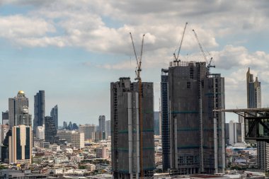 Bangkok, Tayland 'daki yüksek binaların tepesinde çalışan büyük inşaat vinçleri ve arka planda hareket eden bulutlar ve yüksek binaların zamanlanmış görüntüsü