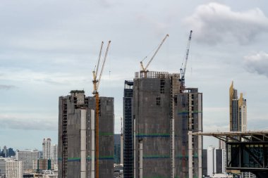 Bangkok, Tayland 'daki yüksek binaların tepesinde çalışan büyük inşaat vinçleri ve arka planda hareket eden bulutlar ve yüksek binaların zamanlanmış görüntüsü
