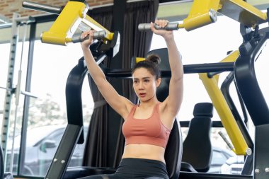 Genç bir kadın spor salonunda sabah antrenmanı sırasında kollarını çalıştırmak için spor makinesini kullanıyor.