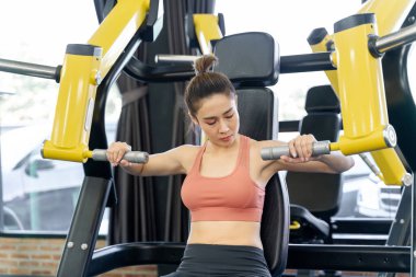 Genç bir kadın spor salonunda sabah antrenmanı sırasında kollarını çalıştırmak için spor makinesini kullanıyor.