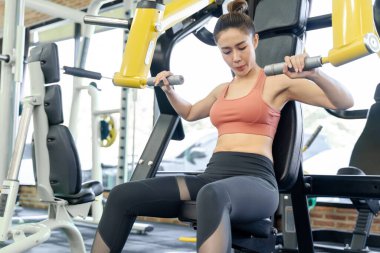 Genç bir kadın spor salonunda sabah antrenmanı sırasında kollarını çalıştırmak için spor makinesini kullanıyor.