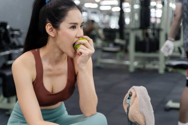 Genç ve güzel bir kadın sabah spor salonunda yeşil elmasını yemek için ara veriyor.