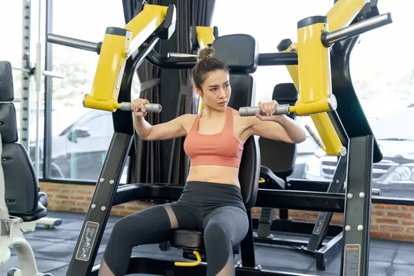 Genç bir kadın spor salonunda sabah antrenmanı sırasında kollarını çalıştırmak için spor makinesini kullanıyor.