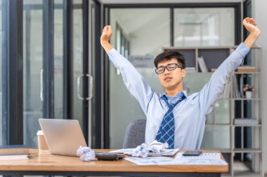 Yorgun ve çok çalışan genç iş adamı ofiste geç saatlere kadar çalışırken kollarını uzatıyor.