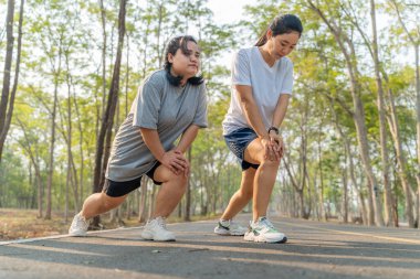 İki genç bayan arkadaş sabah koşularına başlamadan önce kollarını ve bacaklarını esnetiyorlar.