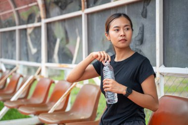 Genç Asyalı bayan koşucu, koşu molası sırasında su şişesinin kapağını açıyor.