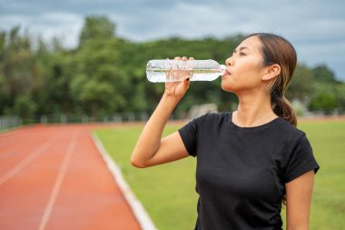 Akşam koşusundan sonra su molası sırasında plastik bir şişeden su içen yorgun genç bir bayan koşucu.