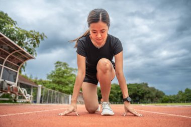 Kararlı kadın koşucu, koşma pozisyonunda çömelmiş bir şekilde koşuya çıkmaya hazırlanıyor.