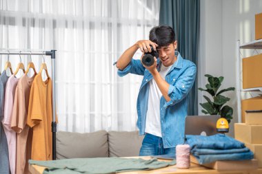 Genç online satıcı web sitesinde kullanmak için gömlek ürününün fotoğraflarını çekiyor ve internet üzerinden ev stüdyosunda inceleme yapıyor.