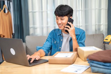 Bilgisayarından gelen siparişleri kontrol ederken müşterisiyle telefonda konuşan mutlu genç satıcı.