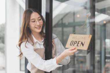 Mutlu genç bayan kahve dükkanı sahibi elini açık tabelayı çevirip dükkanını müşterilerine açmak için kullanıyor.