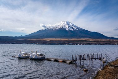 Kawaguchiko Gölü 'ndeki Fuji Dağı' nın arka plandaki bulutları ve kürek çeken kuğu teknelerinin görüntüsü