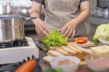Önlüklü bir kadın şef, ahşap bir kesme tahtasının üzerinde diğer malzemelerle birlikte taze yeşil marul düzenliyor. Sağlıklı beslenme, yemek hazırlama ya da aşçılık sanatları için birebirdir.