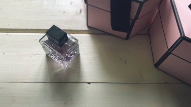 Pencereden gelen ışıkla aydınlatılmış beyaz tahta arka planında hediyeler olan bir parfüm şişesi.