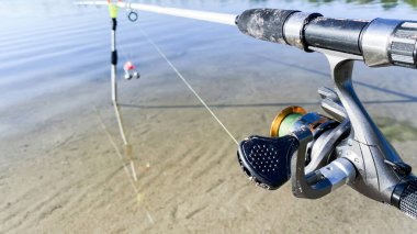 Nehrin kıyısında, iki oltayla balık avlıyoruz. Besleyici aygıtı, beyaz