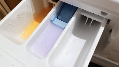 Bir çamaşır tozu tepsisinin üç bölmesi çok renkli sıvı deterjanlarla doludur. Üst manzara, plastik tepsi