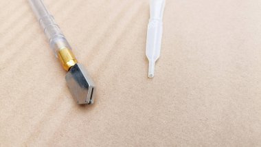 Metal uçlu cam kesici ve plastik pipet bej arka planda yer almaktadır.