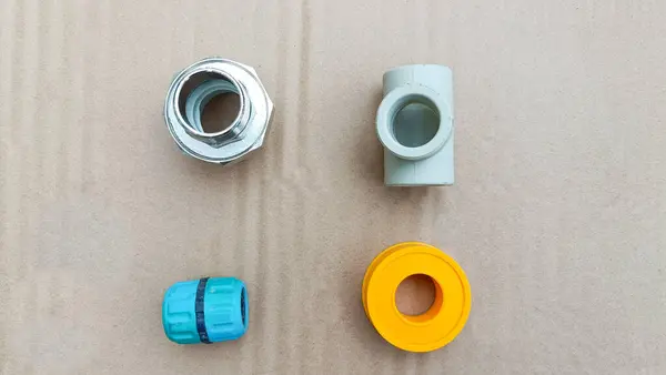 Dört tesisat tesisatı ve bir rulo bant bej arka planda, metal ve plastikten yapılmış, turuncu bantla düzenlenmiş.