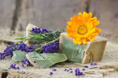 Kaba ahşap arka planda doğal el yapımı sabun, lavanta ve otlar.