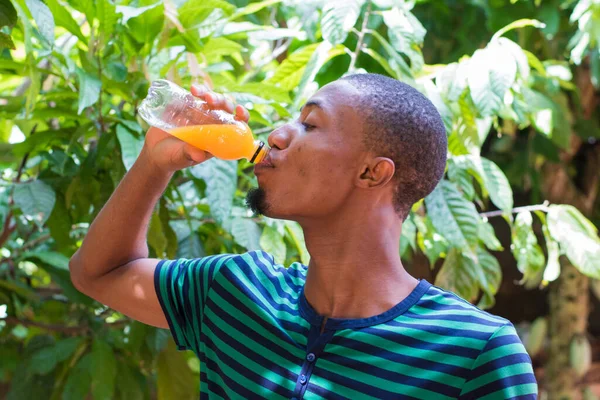 A handsome fair complexion African Nigerian male man drinking an orange juice from a transparent bottle with eyes closed from enjoying the refreshing drink
