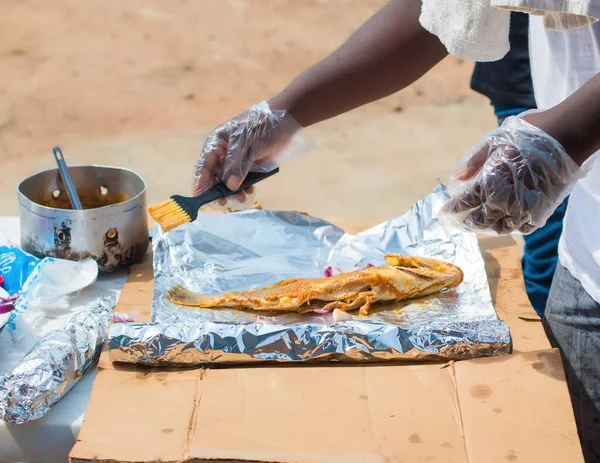 Hands of an African Nigerian chef wearing transparent nylon gloves, preparing grilled fish with relevant ingredient while onions and ginger are part of the spices