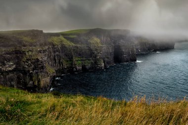 Moher 'in ünlü uçurumlarının puslu manzarası ve vahşi Atlantik Okyanusu, County Clare, İrlanda.