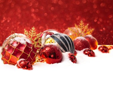 Kırmızı arka planda karda bir sürü Noel topu var.