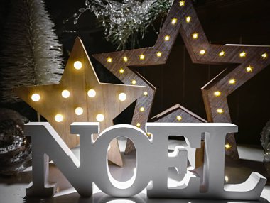 Yıldızlarla aydınlatılmış arka plandaki ahşap harflerden yapılmış Noel kelimesi. Noel süslemesi.