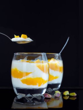 Sağlıklı kahvaltı. Yunan yoğurdu ve mango parçaları siyah teknede fıstıklı bardaklarda.