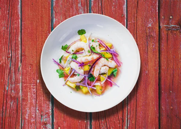 Limon suyunda marine edilmiş taze balık tabağı. Kırmızı ahşap masada karides ve Mango Ceviche. Diyet ve sağlıklı gıda konsepti